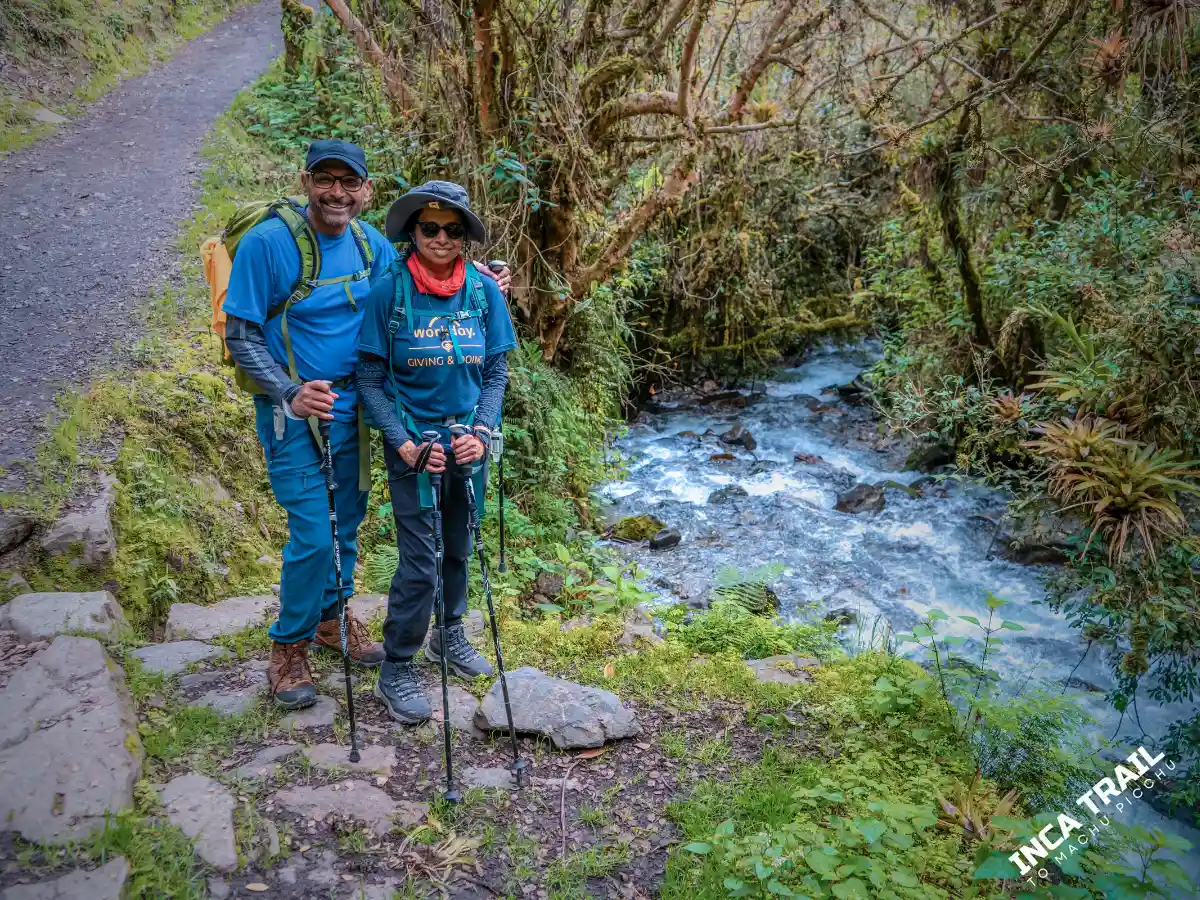 Pareja recorriendo el Camino Inca en temporada seca, atravesando un tramo verde de montaña con clima más despejado.