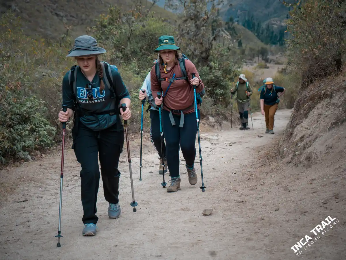 Viajeros caminando por el Camino Inca en un tramo amplio de montaña, con equipo de trekking y paso sostenido.