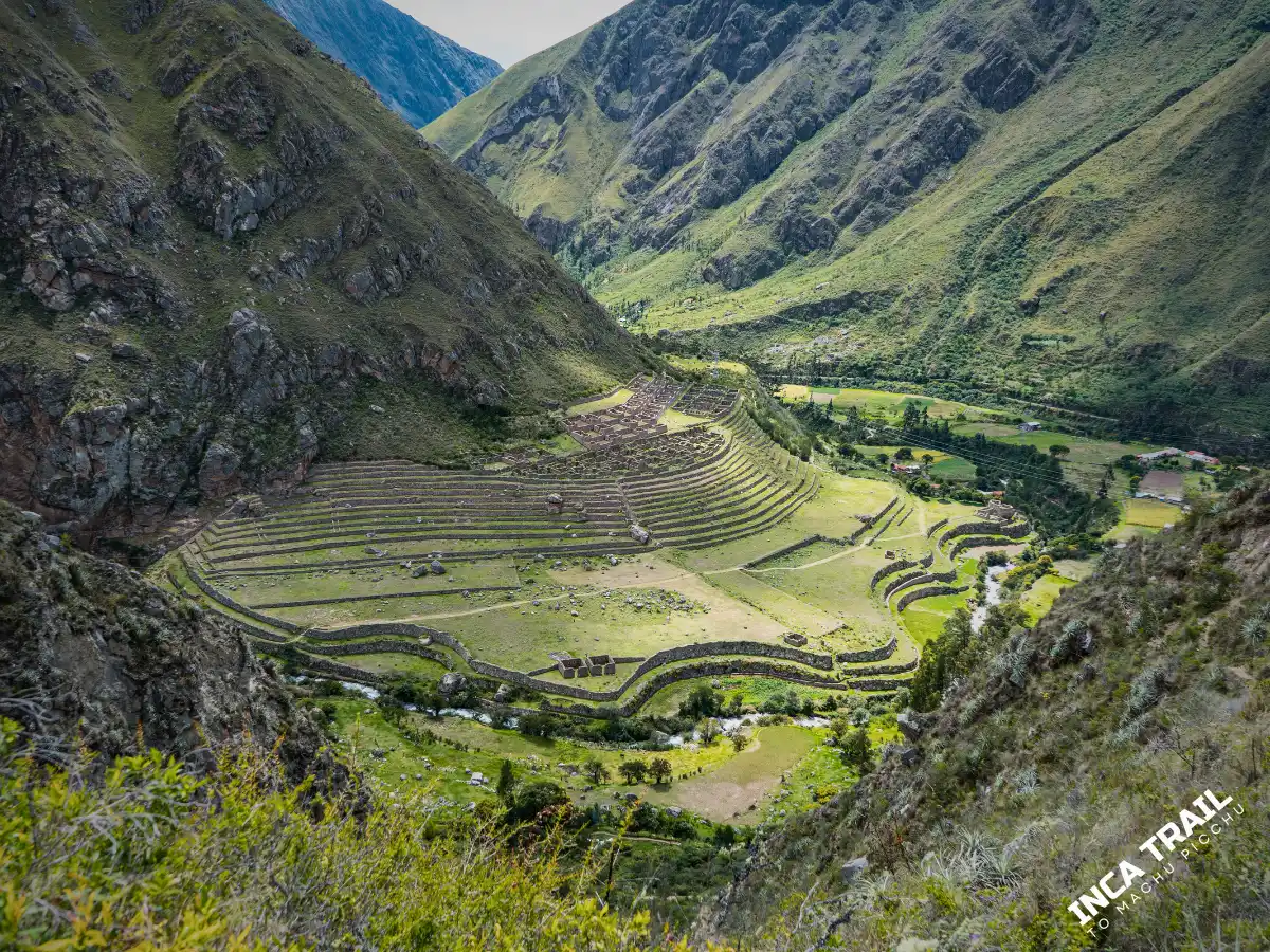 Wide view of Patallacta archaeological site with Inca terraces and stone structures on a green mountainside along the Inca Trail.
